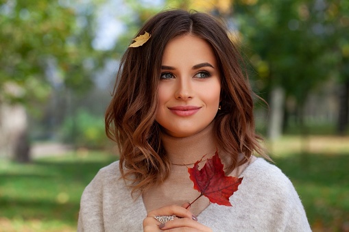 Portrait of happy pretty woman holding red maple leaf outdoor