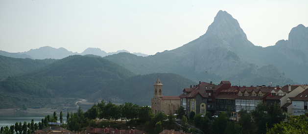 View of misty Riaño village in León, Spain. The parish church of Santa Águeda and hotel buildings in the foreground and Peak Gilbo in the background.