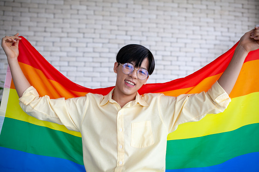 Asian gay holding lgbt rainbow flag at home,  LGBTQ concept.