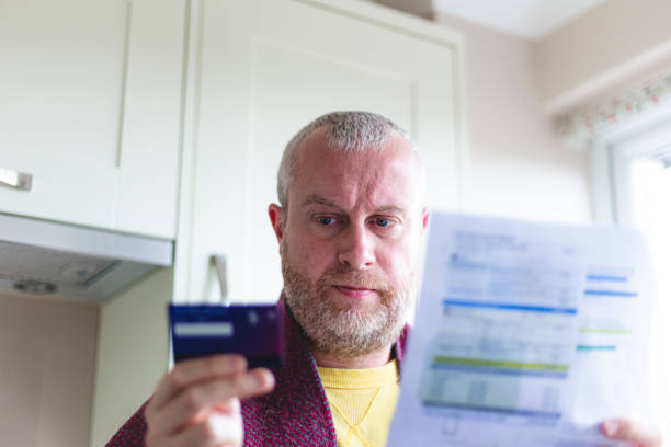 istock Cold man wearing blanket paying heating bill using mobile phone and credit card 1419336274