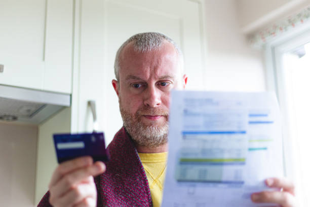 istock Cold man wearing blanket paying heating bill using mobile phone and credit card 1419336277
