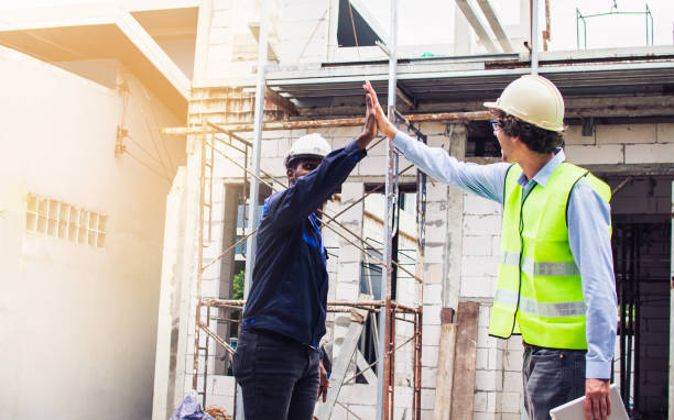 istock Two diversity male engineers team working, inspecting outdoor at construction site, wearing hard hats for safety, giving high five, handshaking for winner and success. Career, Industry Concept. 1419338747