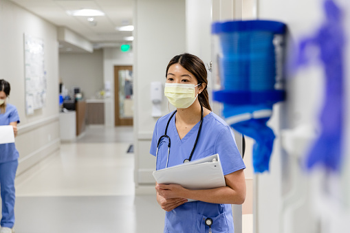 The nurse stands in the hallway holding onto the medical chart waiting for the doctor to arrive to the patient's room.