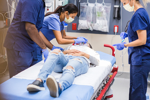 The mature adult female nurse administers oxygen while the rest of the team prepares to examine the emergency patient.