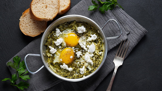 Green shakshuka with spinach, and feta in a frying pan on a table with bread