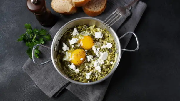 Photo of Green shakshuka with spinach, and feta in a frying pan on a table with bread