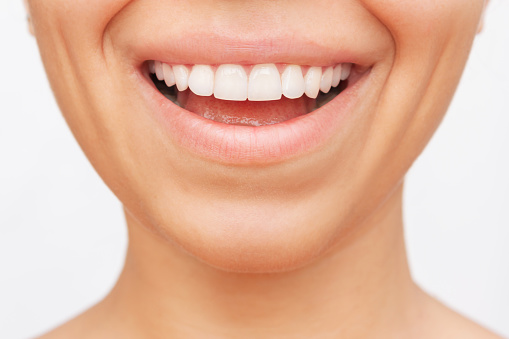 Cropped shot of a young caucasian smiling woman demonstrating perfect white even teeth isolated on a white background. Oral hygiene, dental health care. Veneers, teeth whitening. Dentistry