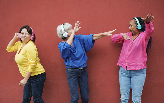 Multiracial senior women dancing to music playlist while wearing wireless headphone