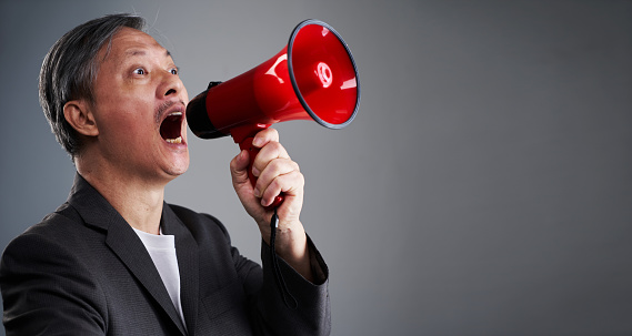 Asian man in business attrie shouting on megaphone isolated on light gray banner background with copy space