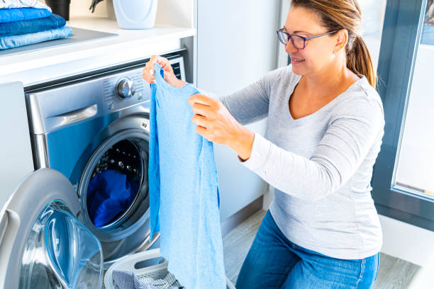Mature smiling woman loading washing machine with laundry at home. Copy space available. High resolution 42Mp indoors digital capture taken with SONY A7rII and Zeiss Batis 40mm F2.0 CF lens