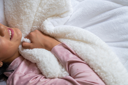 Average 25 year old Latina dressed in pajamas enjoying her quiet time lying under her beautiful sheets