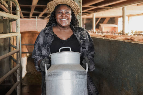 jovem agricultor africano mulher sorrindo na câmera dentro de galpão enquanto segurava lata de leite - farmer color image photography switzerland - fotografias e filmes do acervo