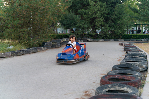 boy driving battery car on karting track. The roadside is covered with tires. The race track, located in the park with trees, was shot with a full frame camera.