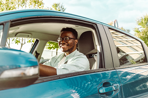 Smiling African-American man in holding the steering wheel and smiling while driving a car