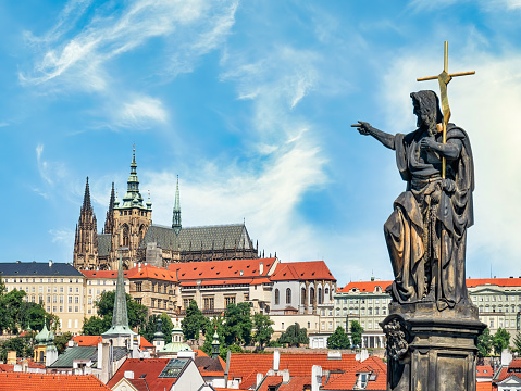 Prague, Czech Republic - June 2022:Statue of a saint on Charles Bridge pointing towards Prague Castel in Czech Republic