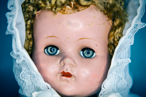 Close-up of beautiful porcelain doll with blond hair and blue eyes, sky blue vintage dress. Little princess games.