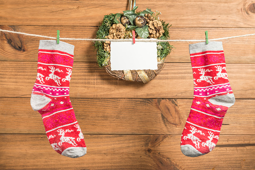 Christmas background with greeting card and a red socks placed on a rope with clothespins with wooden boards in the background.