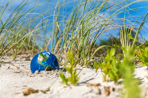 Planet Earth in the hot dunes of a beach. Conceptual image about global droughts as a result of climate change. \nVisual references from NASA (https://visibleearth.nasa.gov/images/74117/august-blue-marble-next-generation).