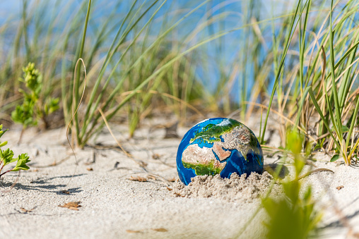 Planet Earth in the hot dunes of a beach. Conceptual image about global droughts as a result of climate change. \nVisual references from NASA (https://visibleearth.nasa.gov/images/74117/august-blue-marble-next-generation).