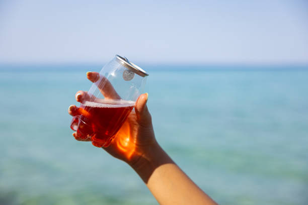 Unrecognizable young Caucasian woman  holding transparent plastic can with ice tea, with a sea as a background