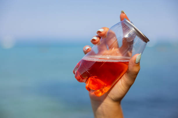 Unrecognizable young Caucasian woman  holding transparent plastic can with ice tea, with a sea as a background