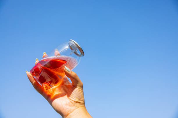 Unrecognizable young Caucasian woman holding transparent plastic can with ice tea with a sky as a background
