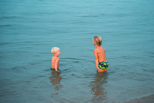 Two beautiful young caucasian kids in the water at the sea. They are bonding, wearing swimsuits and enjoying a fresh afternoon at the beach.