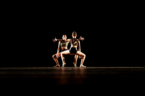 Girl duet performing contemporary dance on dark stage