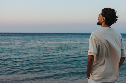 A young man is standing next to the sea looking into the distance with copy space,