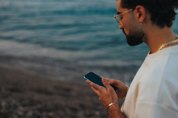 istock Stylish man with cellphone on beach. 1419375912
