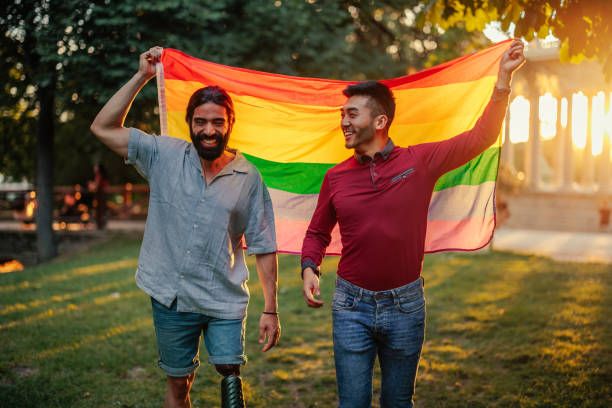 bisexual male couple outdoors with rainbow flag - parade rest imagens e fotografias de stock