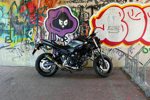 Rheine, NRW, Germany - August 24 2022 A black Suzuki SV650 motorcycle standing in front of a graffiti wall. A bicycle stand at the right