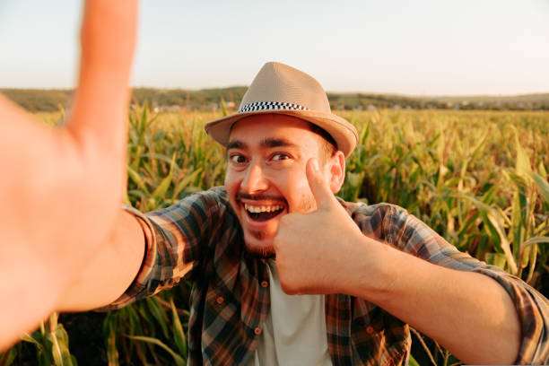 istock Crazy young farmer stand in field, makes faces, looking at camera, front view, thumb up. 1419382867