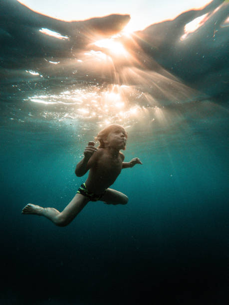 Young blond caucasian boy diving and exploring underwater on a beautiful day at the beach. He is wearing swimwear and holding his breath.