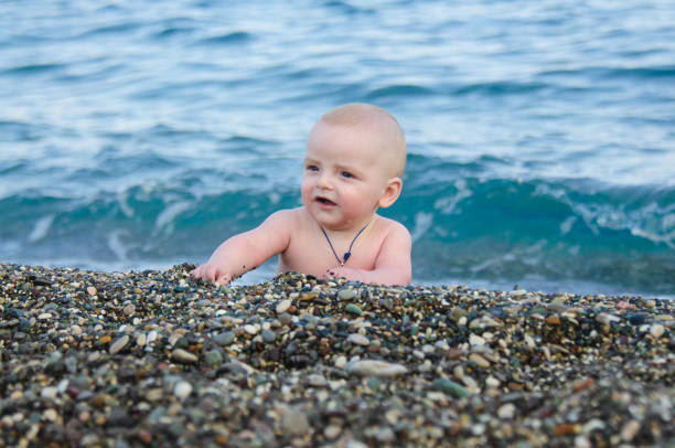 A small child on the beach of pebbles. In the background is a blue sea out of focus and with waves.