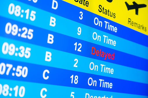 Looking up at a close-up of a Departure Board monitor at a flight “Delayed”.