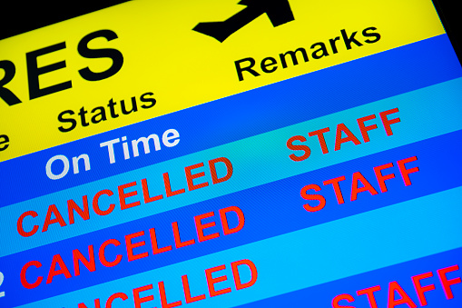 Looking up at a close-up of a Departure Board monitor with a flight cancelled because of no crew.