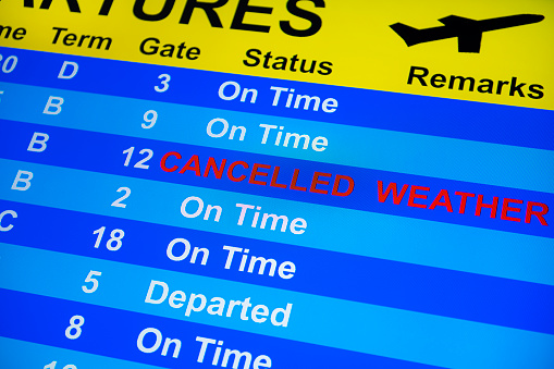 Looking up at a close-up of a Departure Board monitor with a flight “Cancelled” of “Weather”.