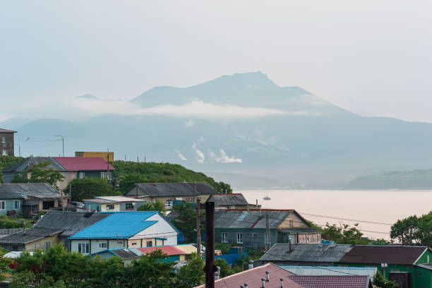 landscape of the town of Yuzhno-Kurilsk on the island of Kunashir with a view of the sea bay and the Mendeleev volcano in the distance landscape of the town of Yuzhno-Kurilsk on the island of Kunashir with a view of the sea bay and the Mendeleev volcano in the distance kunashir island stock pictures, royalty-free photos & images