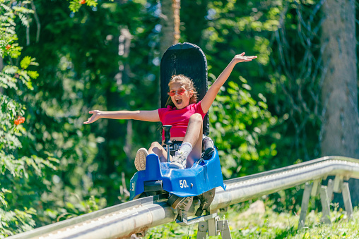 Screaming girl riding mountain roller coaster with outstretched arms. Forest in background