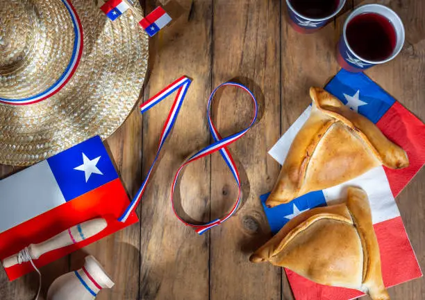 Photo of Chilean independence day concept. fiestas patrias. Tipical baked empanadas, wine or chicha, fat and play emboque. Decoration for 18 september party day, wooden background, top view