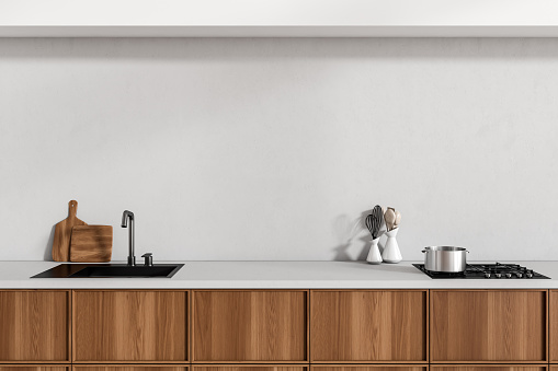 Close up view on bright kitchen room interior with cupboard, white empty wall, sink, gas cooker, spoon, cooking desks. Concept of minimalist design. 3d rendering