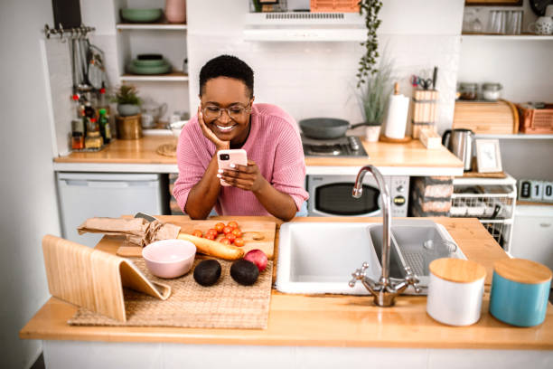 istock Young millennial woman using phone in kitchen while preparing lunch 1419405602
