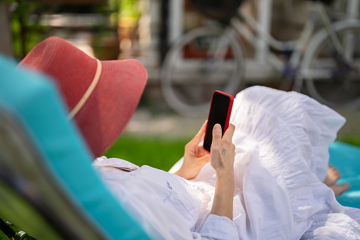 Woman with red hat using mobile phone on sunbed