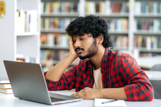 istock Chronic sleep deprivation. Tired bored arabian or indian university student, is sleeping while sitting at desk in library, exhausted of learning, preparing for exam session, suffering of lack of sleep 1419416548