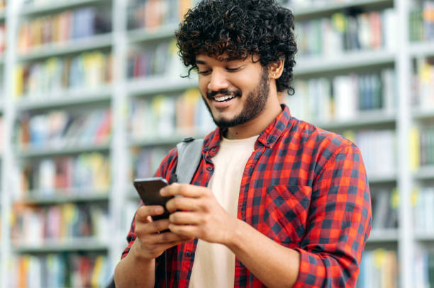 istock Happy indian or arabian millennial guy, freelancer or student, using his smartphone, chatting with friends on social networks, texting sms, browses internet,smile friendly. Wireless technology concept 1419416602