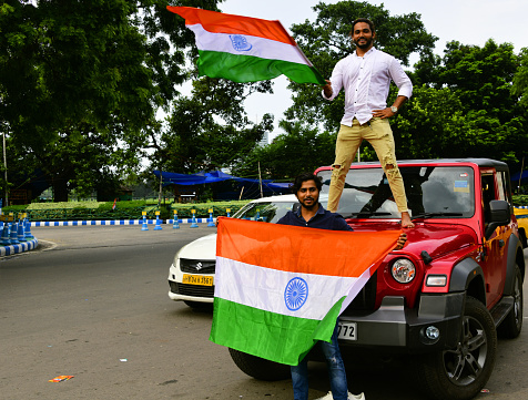 Kolkata / Calcutta, West Bengal, India: cheerful young Indians celebrate independence day (August 15), patriots / nationalist on the street with Indian flags - man atop a Jeep.