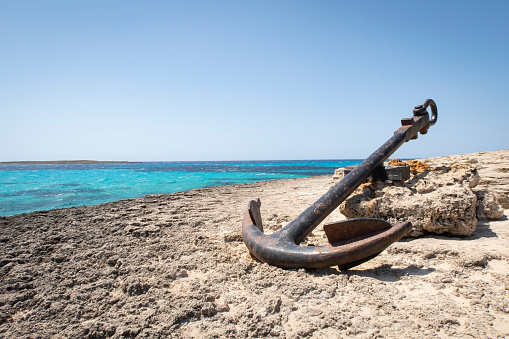a large old anchor, stranded on a rocky cliff with a sea of turquoise water, copy space