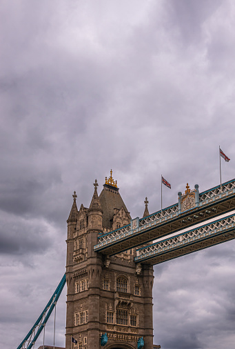 London, England, UK - July 6, 2022: Closeup of northern tower top section at Tower bridge seen from up brown water Thames on Western side under thick gray cloudscape.