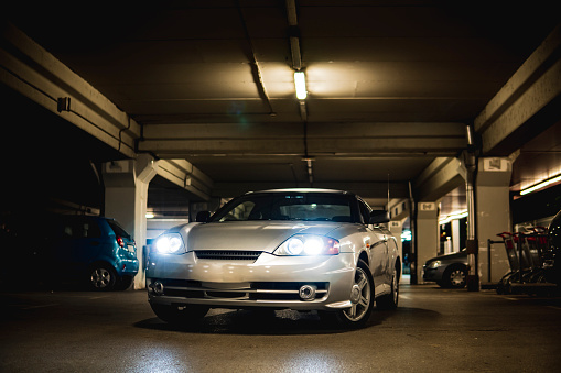 Picture of a gray sports car in the garage with lights on.
